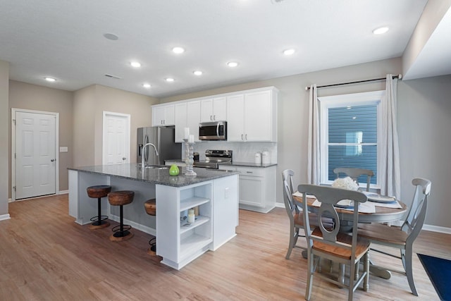 kitchen featuring dark stone countertops, an island with sink, stainless steel appliances, decorative backsplash, and white cabinets