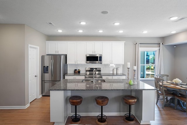 kitchen with appliances with stainless steel finishes, sink, dark stone countertops, white cabinets, and a kitchen breakfast bar