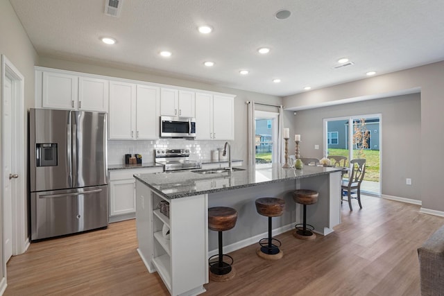 kitchen with appliances with stainless steel finishes, white cabinetry, sink, dark stone countertops, and a center island with sink