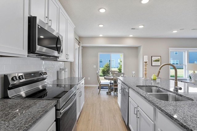 kitchen featuring sink, dark stone counters, white cabinets, stainless steel appliances, and backsplash