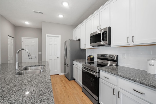 kitchen with sink, white cabinetry, light wood-type flooring, appliances with stainless steel finishes, and dark stone counters