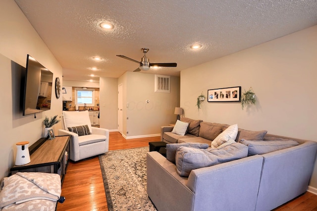 living room with ceiling fan, a textured ceiling, and light hardwood / wood-style floors