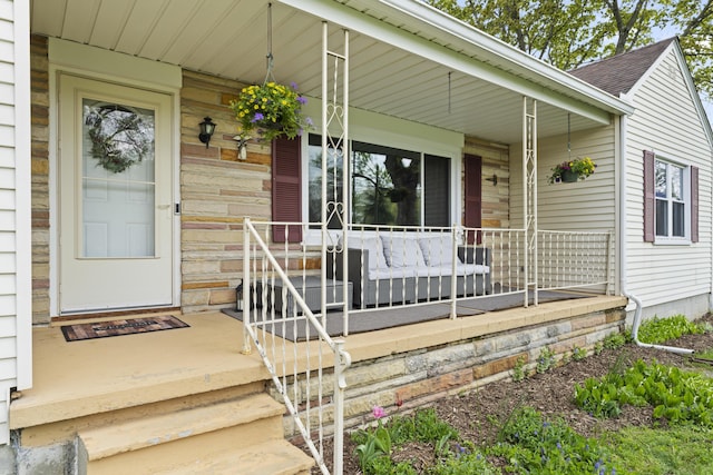 view of exterior entry with a porch, a shingled roof, and stone siding