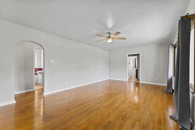 unfurnished room with arched walkways, a ceiling fan, baseboards, and light wood-style floors