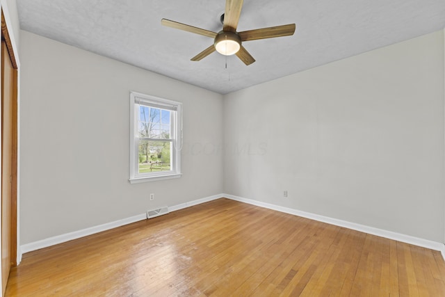 empty room with baseboards, ceiling fan, light wood-type flooring, and visible vents