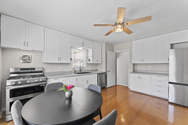 kitchen with appliances with stainless steel finishes, a sink, light countertops, a ceiling fan, and white cabinetry