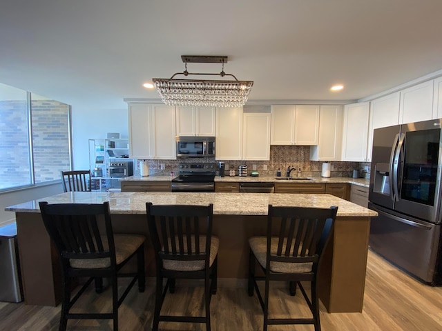 kitchen with stainless steel appliances, white cabinetry, a kitchen island, and light stone countertops