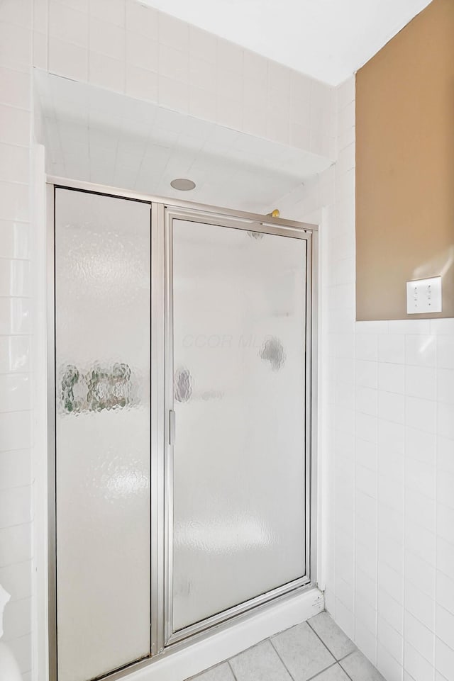 bathroom featuring tile patterned floors, a shower with door, and tile walls