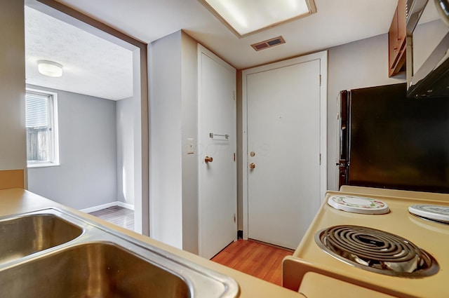 kitchen with sink, light hardwood / wood-style flooring, range, a textured ceiling, and black fridge