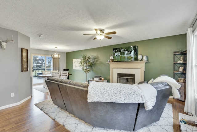 living room featuring a tiled fireplace, wood-type flooring, a textured ceiling, and ceiling fan