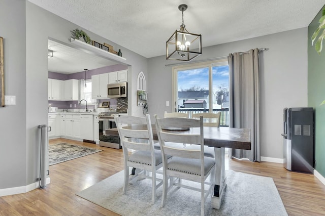 dining room featuring sink, light hardwood / wood-style flooring, a chandelier, and a textured ceiling