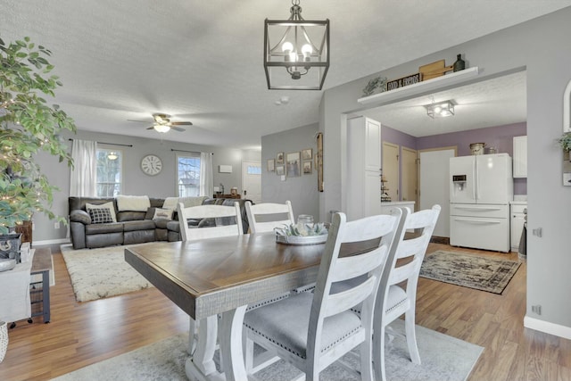 dining space with ceiling fan with notable chandelier, a textured ceiling, and light hardwood / wood-style floors