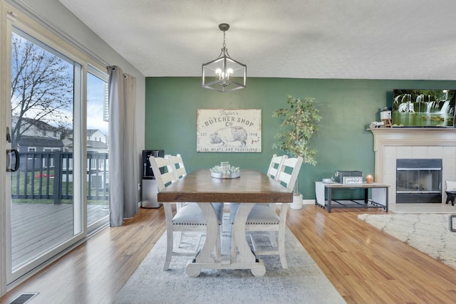 dining area featuring a tiled fireplace, hardwood / wood-style floors, a textured ceiling, and a chandelier