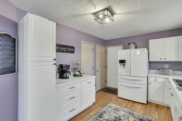 kitchen featuring white cabinets, light hardwood / wood-style floors, a textured ceiling, and white fridge with ice dispenser