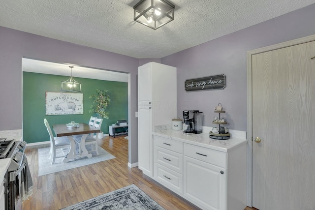 kitchen featuring white cabinetry, decorative light fixtures, a textured ceiling, and light wood-type flooring