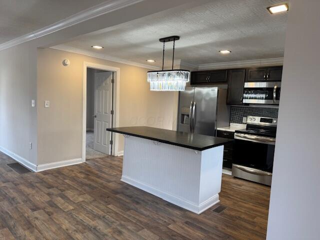 kitchen with dark hardwood / wood-style flooring, ornamental molding, a center island, and appliances with stainless steel finishes