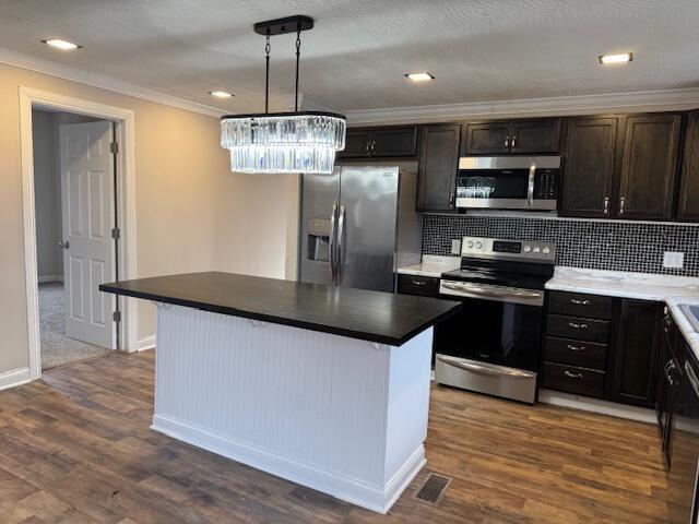 kitchen featuring pendant lighting, dark hardwood / wood-style flooring, ornamental molding, a center island, and stainless steel appliances