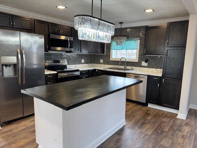 kitchen featuring sink, decorative light fixtures, appliances with stainless steel finishes, dark hardwood / wood-style floors, and a kitchen island