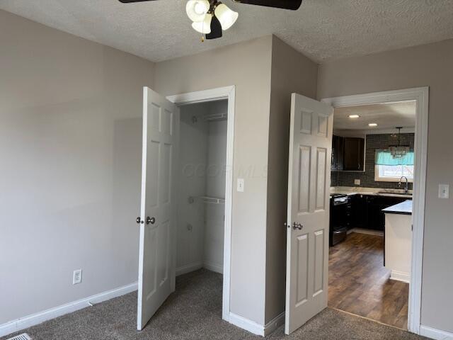 unfurnished bedroom featuring sink, a spacious closet, a textured ceiling, and ceiling fan