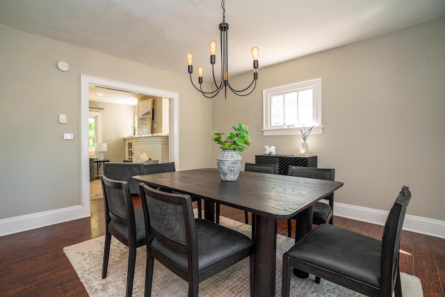 dining area featuring dark wood-type flooring, a notable chandelier, and a fireplace