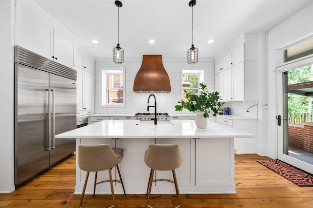 kitchen with white cabinetry, hanging light fixtures, an island with sink, and stainless steel built in refrigerator