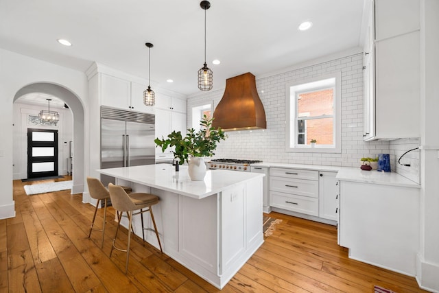 kitchen with premium range hood, white cabinetry, a center island with sink, built in fridge, and stove