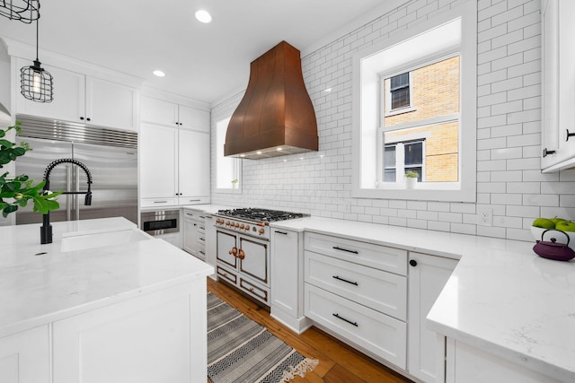 kitchen with custom range hood, stainless steel appliances, light stone countertops, decorative backsplash, and white cabinets