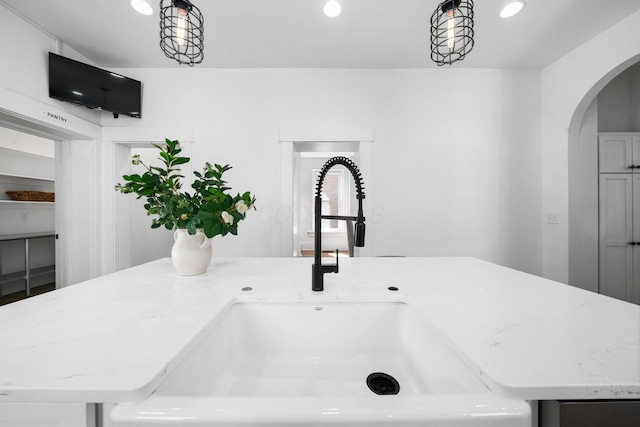 interior details featuring light stone counters, hanging light fixtures, sink, and a kitchen island