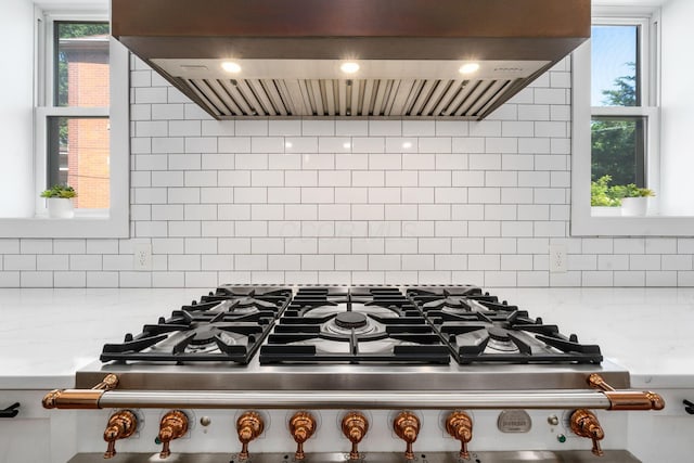 interior details with ventilation hood, stovetop, light stone countertops, and backsplash