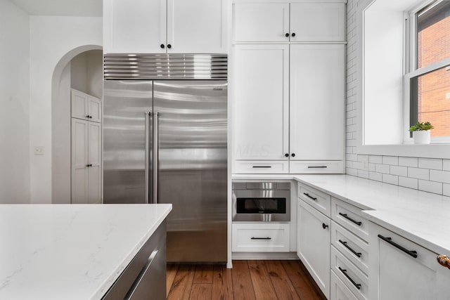 kitchen featuring dark wood-type flooring, white cabinetry, light stone counters, tasteful backsplash, and stainless steel built in fridge