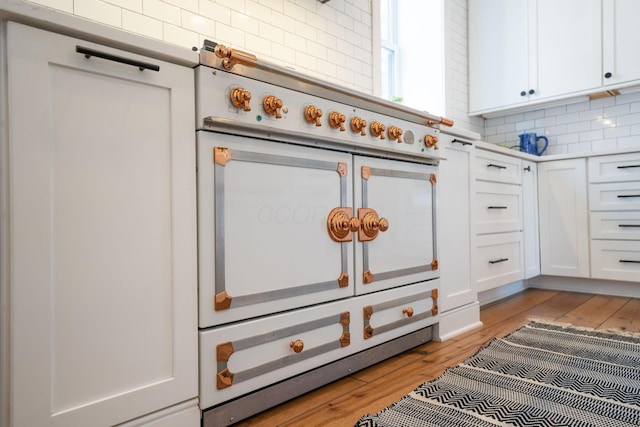 interior details with backsplash, light wood-type flooring, range with two ovens, and white cabinets