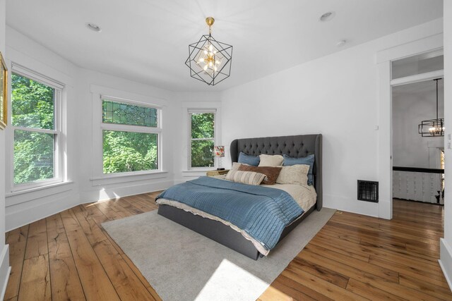 bedroom featuring multiple windows, a notable chandelier, and hardwood / wood-style floors