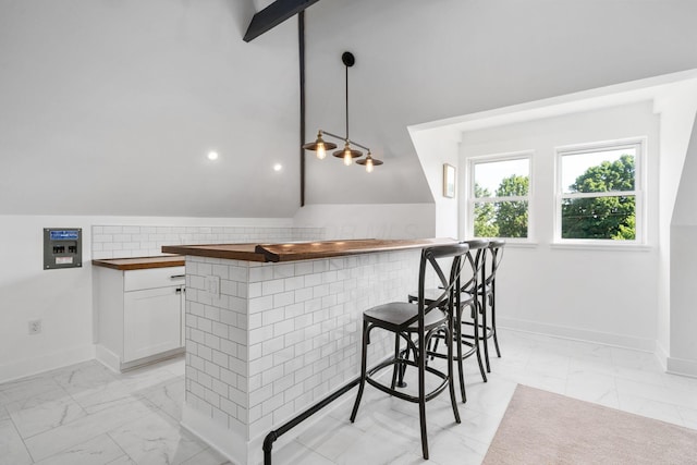 kitchen featuring white cabinetry, lofted ceiling, wooden counters, a kitchen breakfast bar, and hanging light fixtures