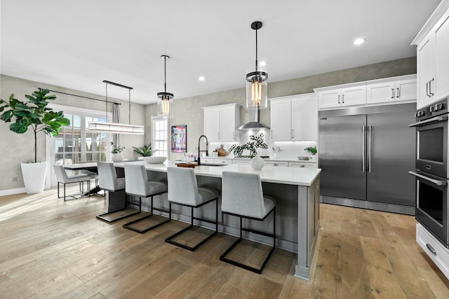 kitchen with sink, light wood-type flooring, appliances with stainless steel finishes, a kitchen island with sink, and white cabinets