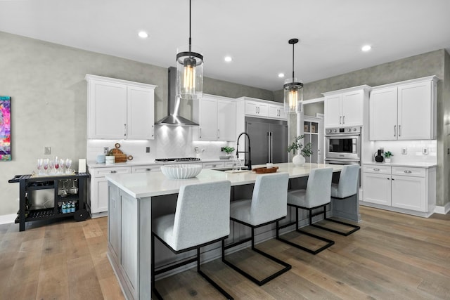 kitchen featuring white cabinetry, decorative light fixtures, stainless steel appliances, and wall chimney exhaust hood