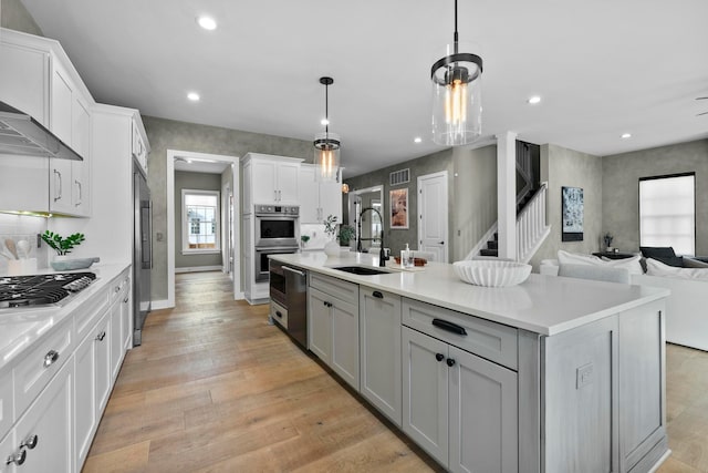 kitchen featuring sink, decorative light fixtures, light hardwood / wood-style flooring, stainless steel appliances, and a kitchen island with sink