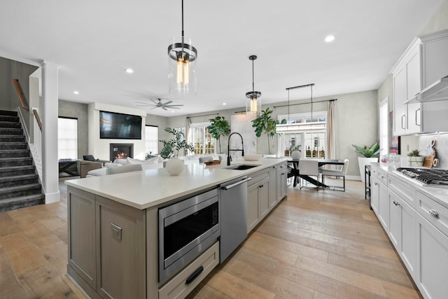 kitchen with sink, decorative light fixtures, an island with sink, stainless steel appliances, and white cabinets