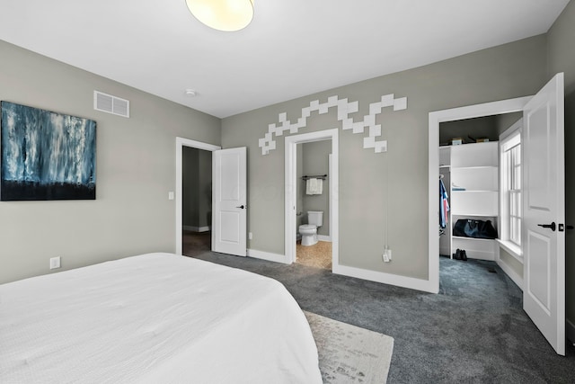 bedroom with a closet, a walk in closet, dark carpet, and ensuite bath