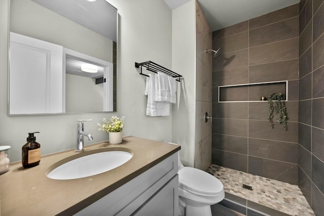 bathroom featuring a tile shower, vanity, and toilet