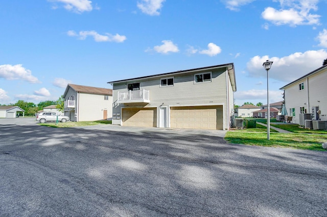 view of front of home with a balcony, a garage, central AC unit, and a front lawn