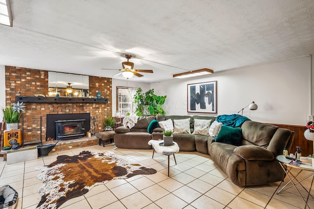 living room featuring light tile patterned floors, a wood stove, a textured ceiling, and ceiling fan