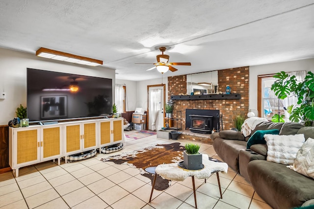 living room with ceiling fan, a wood stove, a textured ceiling, and light tile patterned flooring