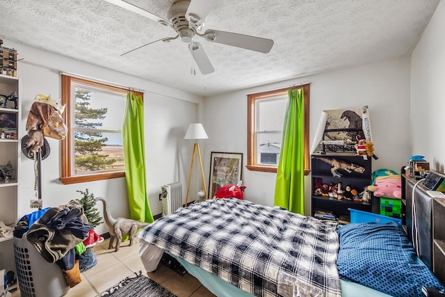 tiled bedroom with multiple windows, radiator, a textured ceiling, and ceiling fan