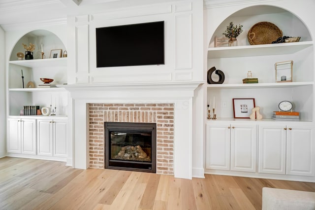 living room with a brick fireplace, built in shelves, and light hardwood / wood-style floors