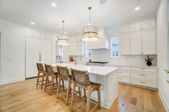 kitchen featuring pendant lighting, a kitchen island with sink, white cabinets, and custom exhaust hood