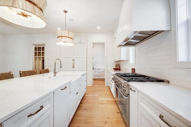 kitchen featuring premium range hood, decorative light fixtures, high end stove, white cabinetry, and light wood-type flooring