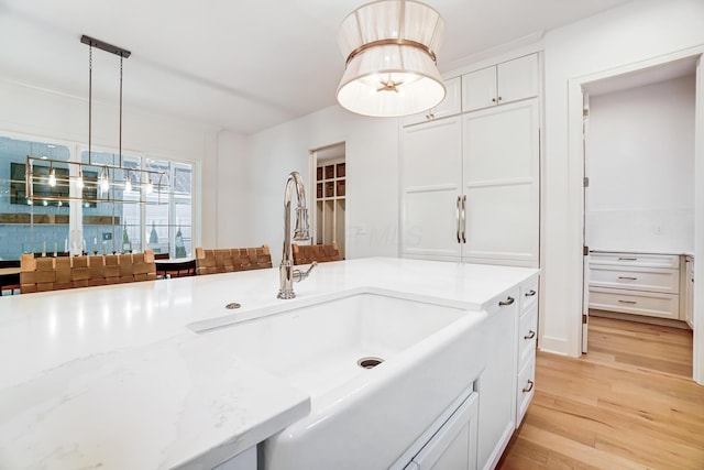 kitchen featuring sink, decorative light fixtures, light wood-type flooring, light stone countertops, and white cabinets