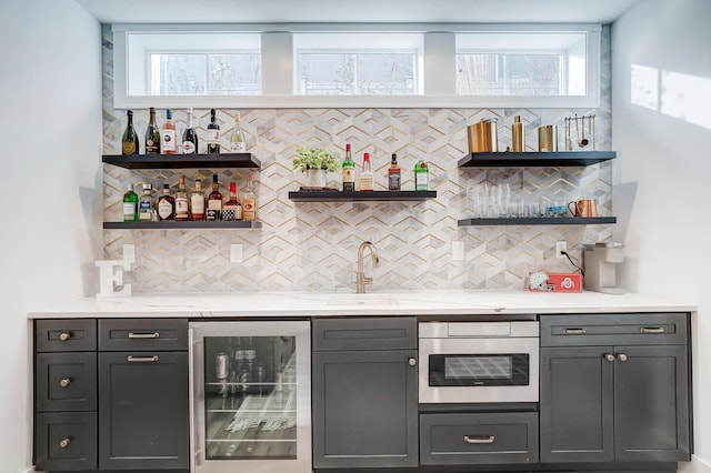 bar with sink, wine cooler, wall oven, light stone counters, and decorative backsplash