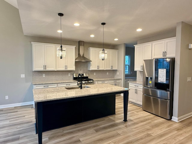 kitchen featuring white cabinetry, hanging light fixtures, appliances with stainless steel finishes, a kitchen island with sink, and wall chimney range hood