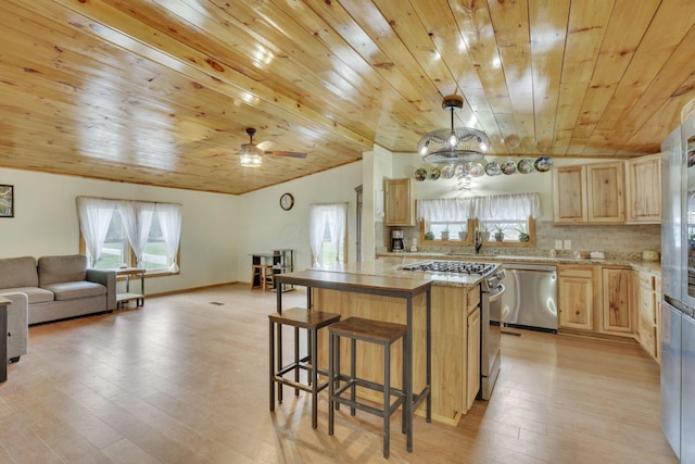 kitchen featuring appliances with stainless steel finishes, hanging light fixtures, tasteful backsplash, a kitchen island, and light wood-type flooring